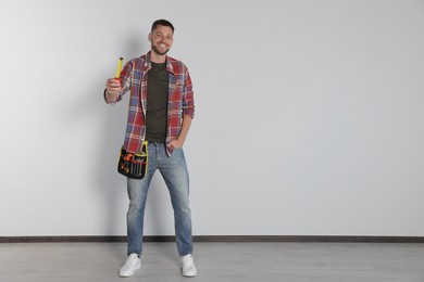 Photo of Handsome worker with measuring tape near white wall, space for text
