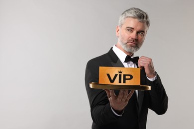 Photo of Handsome man holding tray with VIP sign on light grey background. Space for text