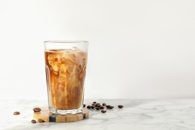 Photo of Refreshing iced coffee with milk in glass and beans on white marble table, space for text