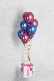 Photo of Bright colorful balloons and gift near brick wall. Party time