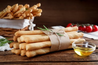 Photo of Delicious grissini sticks, oil, rosemary and tomatoes on wooden table