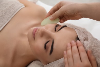 Photo of Young woman receiving facial massage with gua sha tool in beauty salon