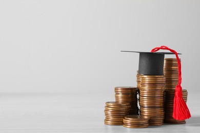 Photo of Scholarship concept. Graduation cap and stacked coins on white wooden table, space for text