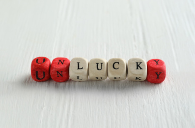 Photo of Red and white cubes with word UNLUCKY on white wooden table, space for text