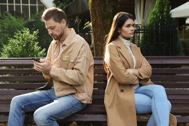 Photo of Upset arguing couple sitting on bench in park. Relationship problems