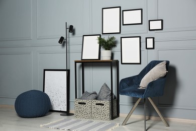 Photo of Stylish room interior with empty frames hanging on grey wall near console table