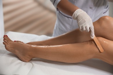 Photo of Professional cosmetologist applying gel on client's leg before laser epilation procedure in salon, closeup