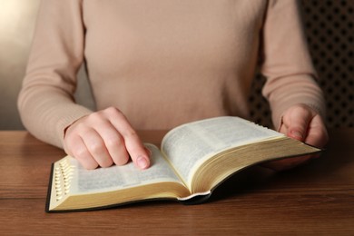Photo of Woman reading Bible at wooden table, closeup