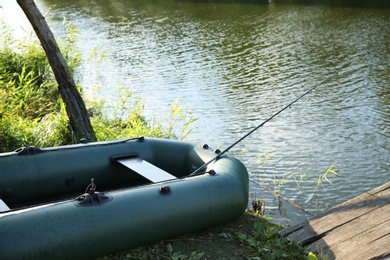 Photo of Inflatable boat with rod for fishing near wooden pier at riverside