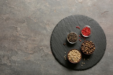 Photo of Slate plate with different types of pepper in bowls on gray background, top view. Space for text