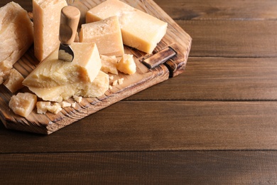 Photo of Pieces of delicious parmesan cheese with knife on wooden table. Space for text