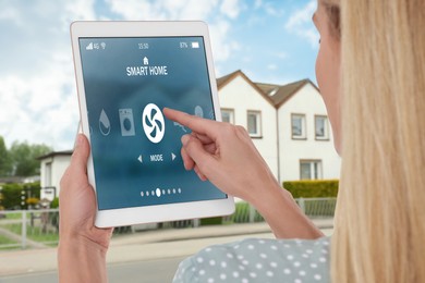 Image of Woman using smart home control system via tablet near house outdoors, closeup