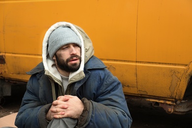 Photo of Poor homeless man sitting near van outdoors