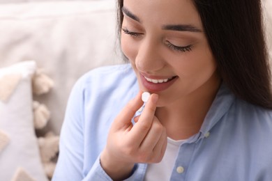 Woman taking pill on blurred background, closeup view