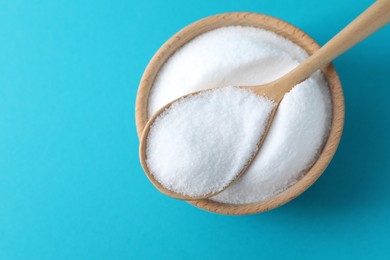 Photo of Organic white salt in bowl and spoon on light blue background, top view. Space for text