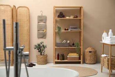 Photo of Shelving unit with soft towels, plants and bottles indoors