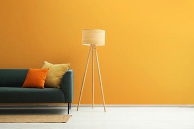 Photo of Stylish sofa with cushions, rug and lamp near orange wall indoors, space for text. Interior design