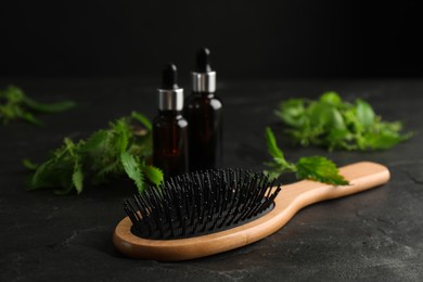 Photo of Stinging nettle leaves, extract and brush on black background. Natural hair care