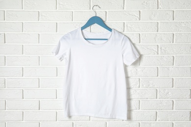 Photo of Hanger with white t-shirt against brick wall. Mockup for design