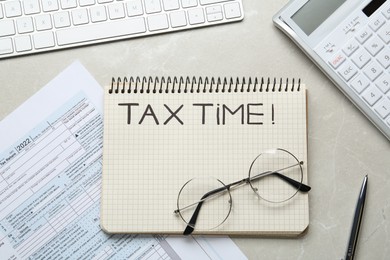 Photo of Notebook with words Tax Time, documents, keyboard, glasses and calculator on grey table, flat lay