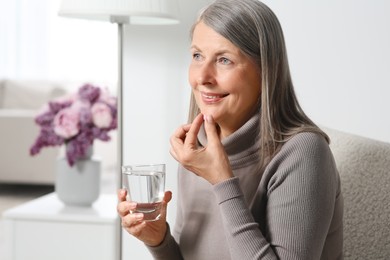 Photo of Senior woman with glass of water taking pill at home. Space for text
