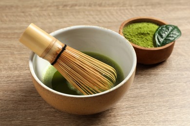 Photo of Cup of fresh matcha tea with bamboo whisk and green powder on wooden table