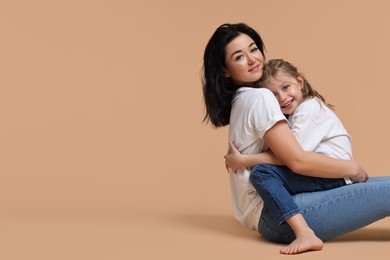 Photo of Beautiful mother with little daughter sitting on beige background. Space for text