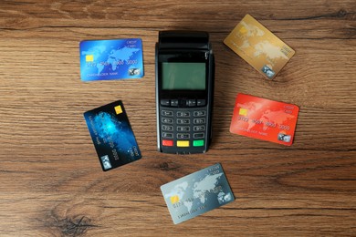 Photo of Modern payment terminal and credit cards on wooden table, flat lay
