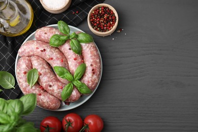 Photo of Raw homemade sausages, basil leaves, tomatoes and spices on grey wooden table, flat lay. Space for text