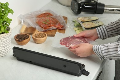 Photo of Woman using sealer for vacuum packing in kitchen, closeup. Sous vide cooking