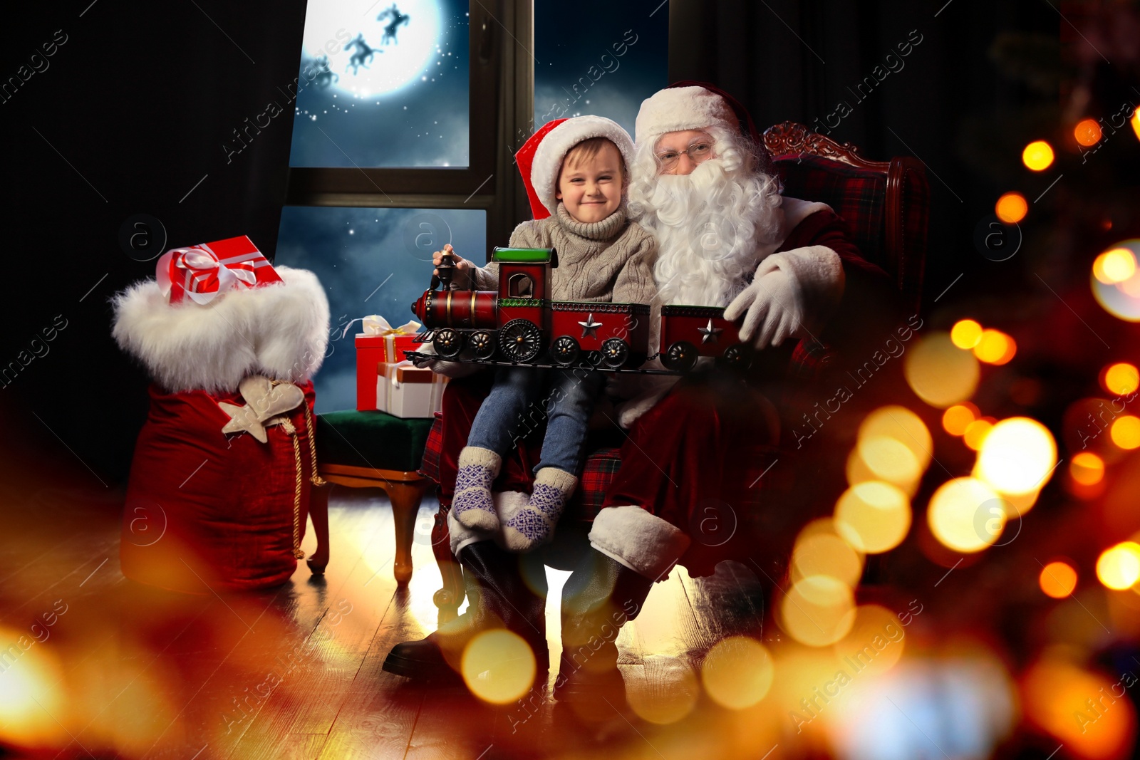 Image of Santa Claus and little boy with toy train near window at home. Christmas holiday