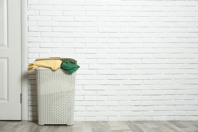 Photo of Plastic laundry basket full of dirty clothes on floor near brick wall. Space for text