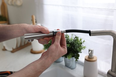 Photo of Plumber examining metal faucet at home, closeup