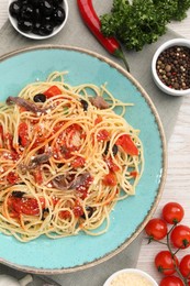 Photo of Plate of delicious pasta with anchovies, tomatoes and parmesan cheese near ingredients on white wooden table, flat lay