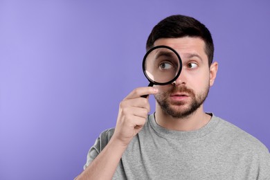 Photo of Man looking through magnifier glass on violet background, space for text