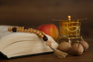 Photo of Bible, rosary beads, walnuts and apple on wooden table, closeup. Lent season