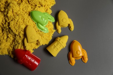 Photo of Different figures made of yellow kinetic sand and plastic toys on grey background, flat lay. Space for text