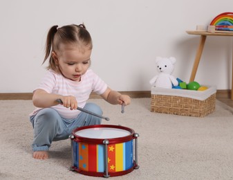 Cute little girl playing with drum and drumsticks at home