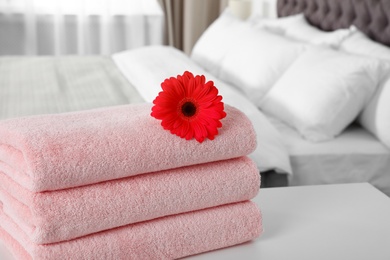 Photo of Stack of fresh towels with flower on table in bedroom. Space for text