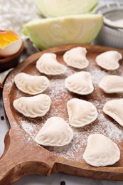 Photo of Raw dumplings (varenyky) with tasty filling and flour on wooden board, closeup