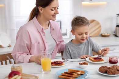 Photo of Mother and her cute little son having breakfast at table in kitchen