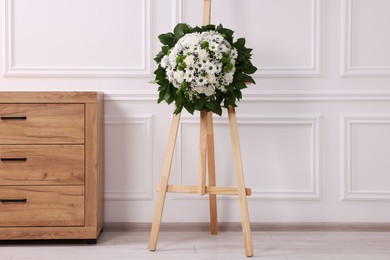 Photo of Funeral wreath of flowers on wooden stand near white wall in room
