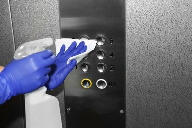 Photo of Woman wiping buttons of elevator`s panel with detergent and paper napkin, closeup