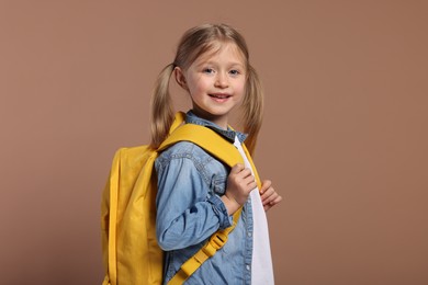Photo of Happy schoolgirl with backpack on brown background