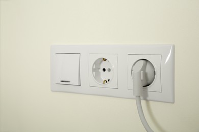 Photo of Power sockets with inserted plug and light switch on white wall indoors