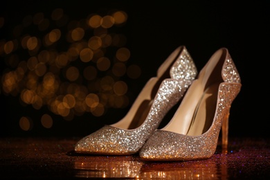 Photo of Golden glitter shoes on dark reflective surface against blurred background. Space for text