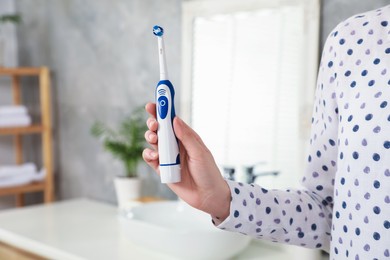Photo of Woman holding electric toothbrush in bathroom at home, closeup