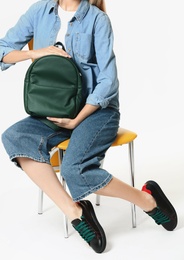 Photo of Woman in stylish shoes with backpack on chair against white background
