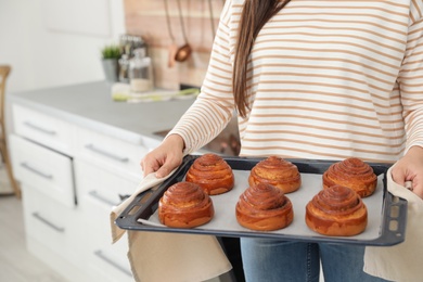 Photo of Young woman with tray of oven baked buns in kitchen, closeup