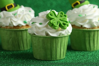 Photo of St. Patrick's day party. Tasty festively decorated cupcakes on shiny green surface, closeup